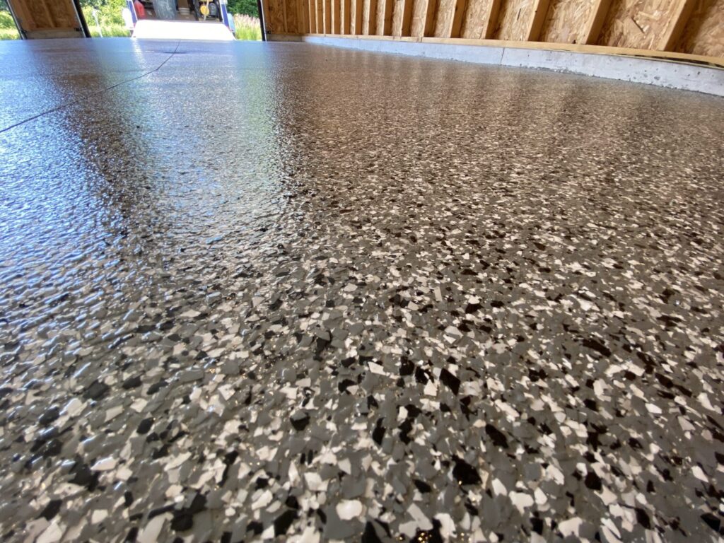A garage with a newly coated, polished speckled floor, featuring open walls and a visible garden area through the doorway.