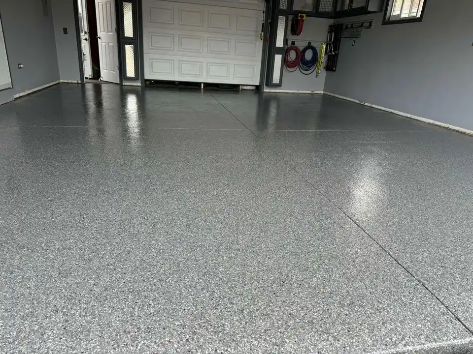 Spacious empty garage with shiny, polished concrete floor and organized storage. Wall hooks hold coiled hoses. White garage door and open entry visible.
