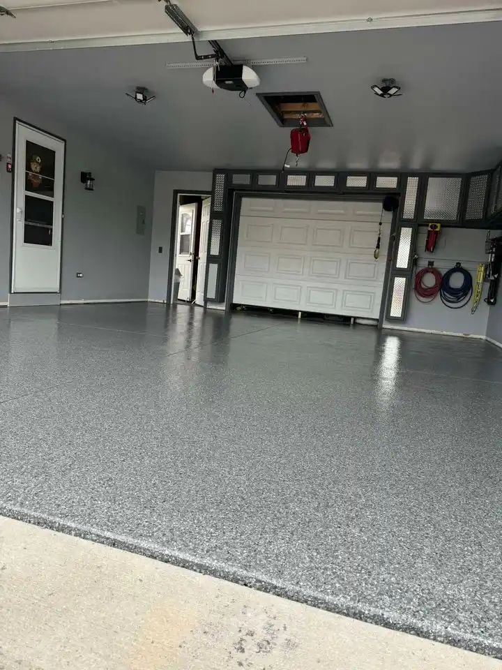 Spacious, modern garage with shiny epoxy floor, organized tools, overhead storage, and large closed door; person smiling through windowed interior door.