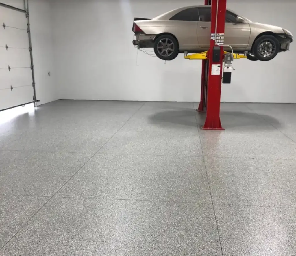 A car is elevated on a red automotive lift inside a spacious, clean garage with a closed white garage door.