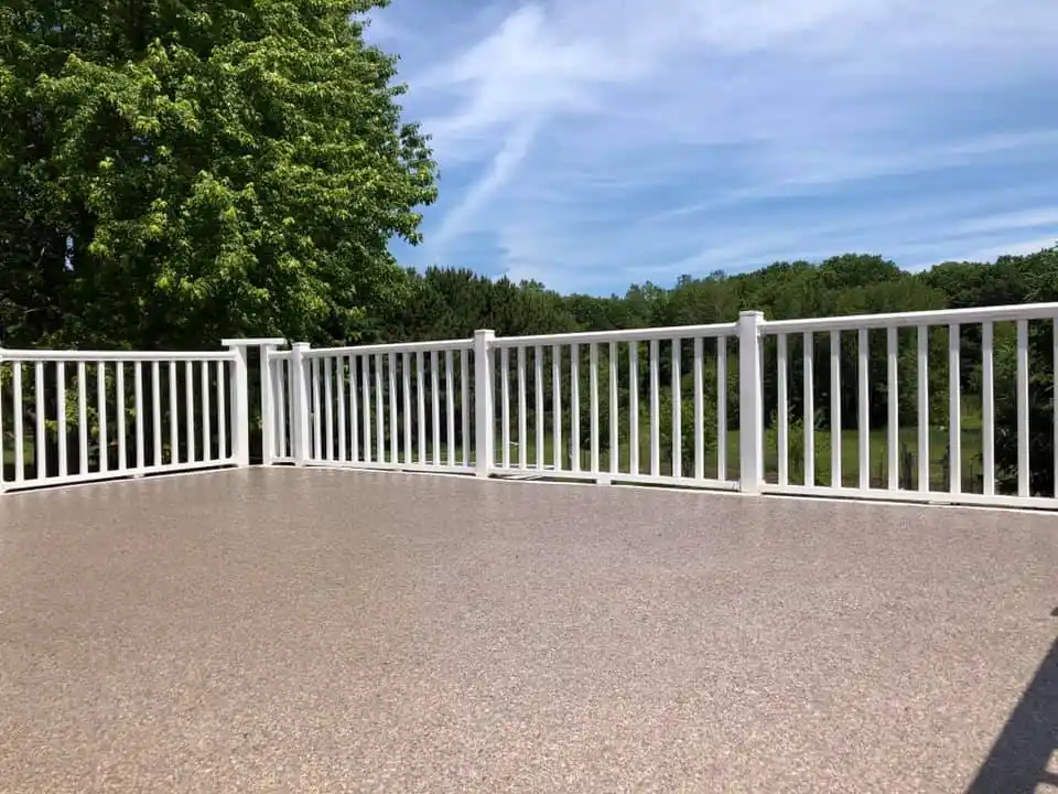 A spacious outdoor deck with white railing overlooks lush green trees and a clear blue sky, creating a serene, open atmosphere.